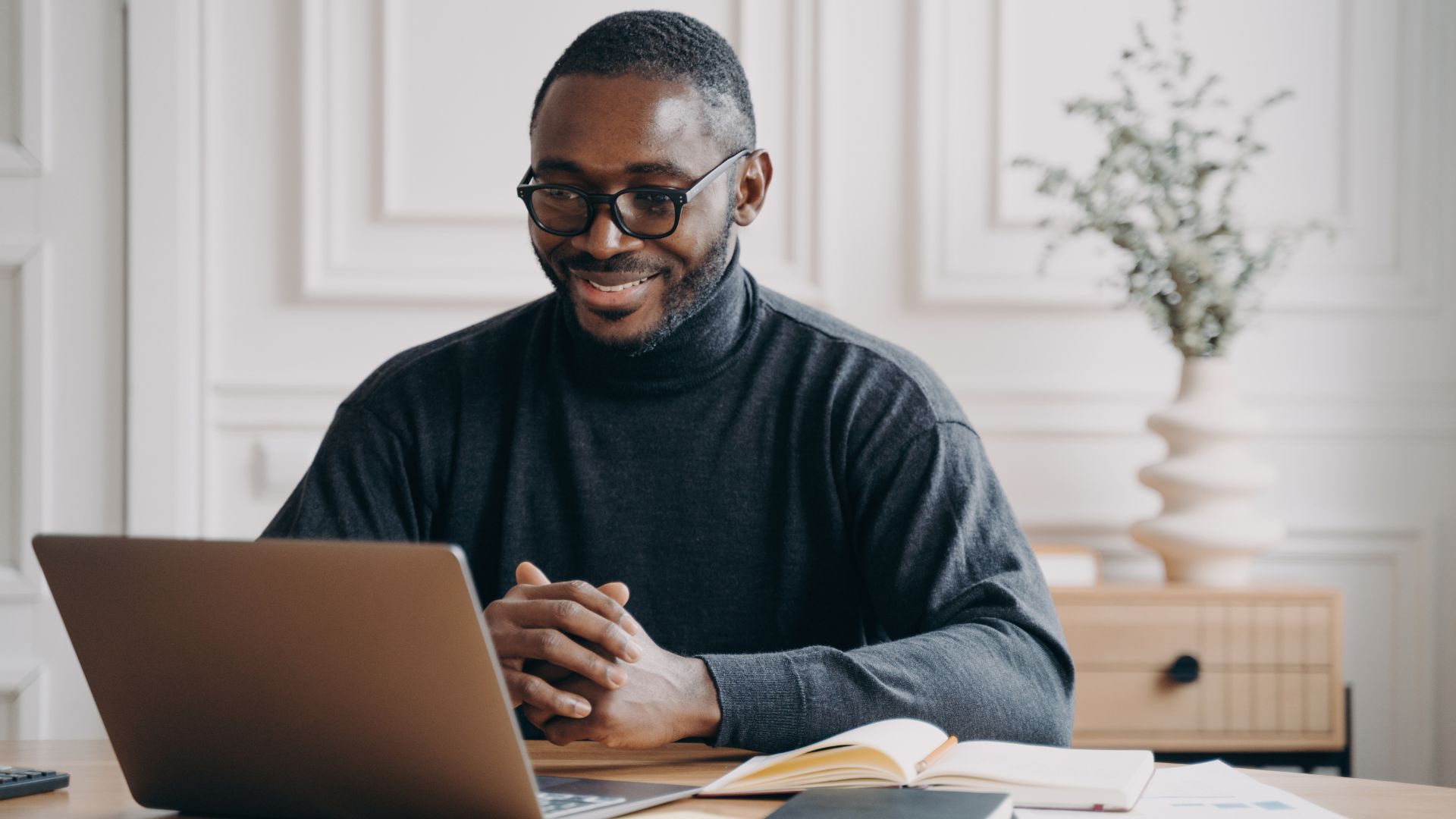 A happy young man is smiling down at his laptop.