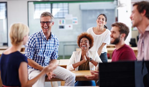 A diverse team is laughing and smiling together in a common work area.