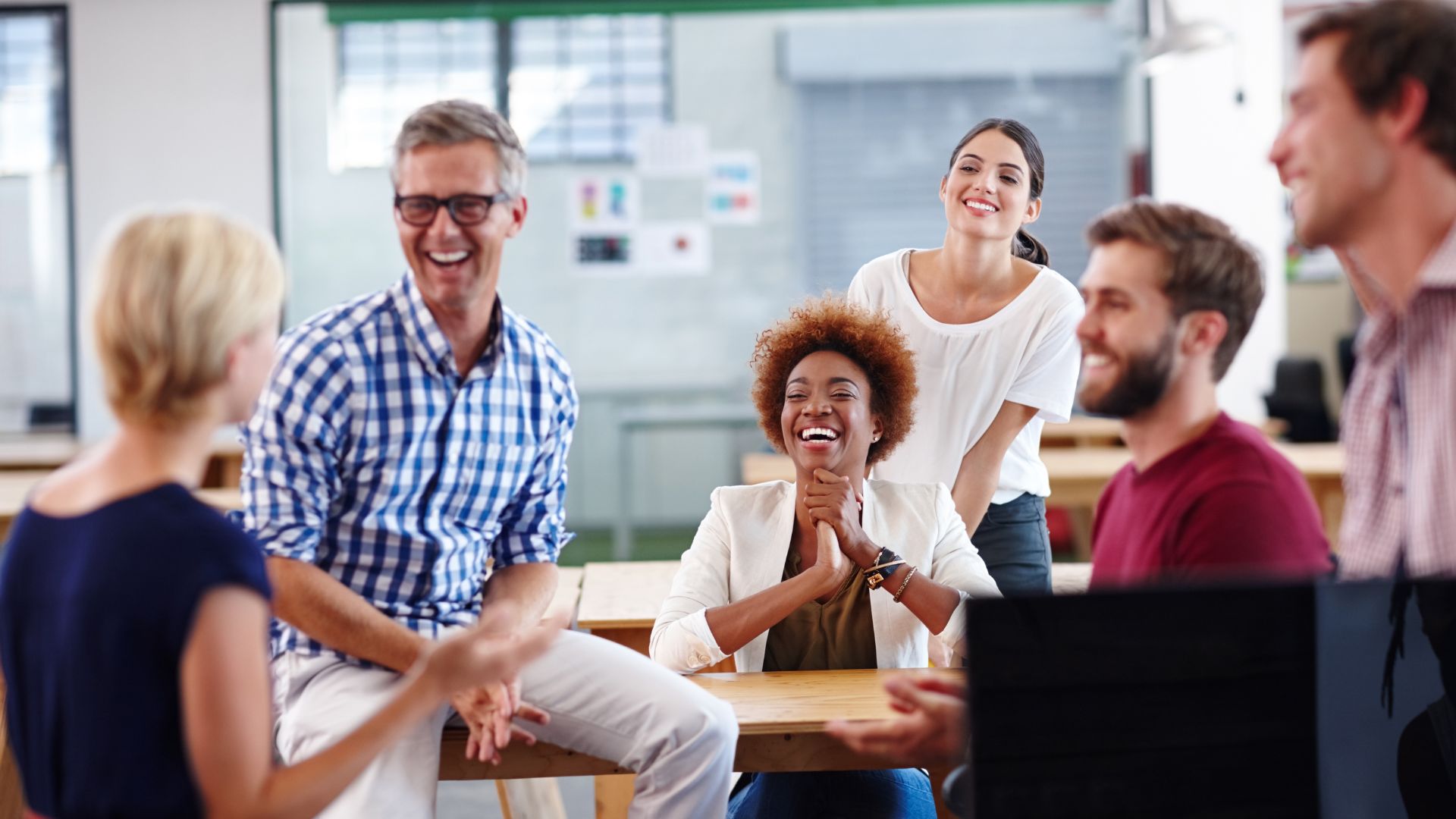 A diverse team is laughing and smiling together in a common work area.