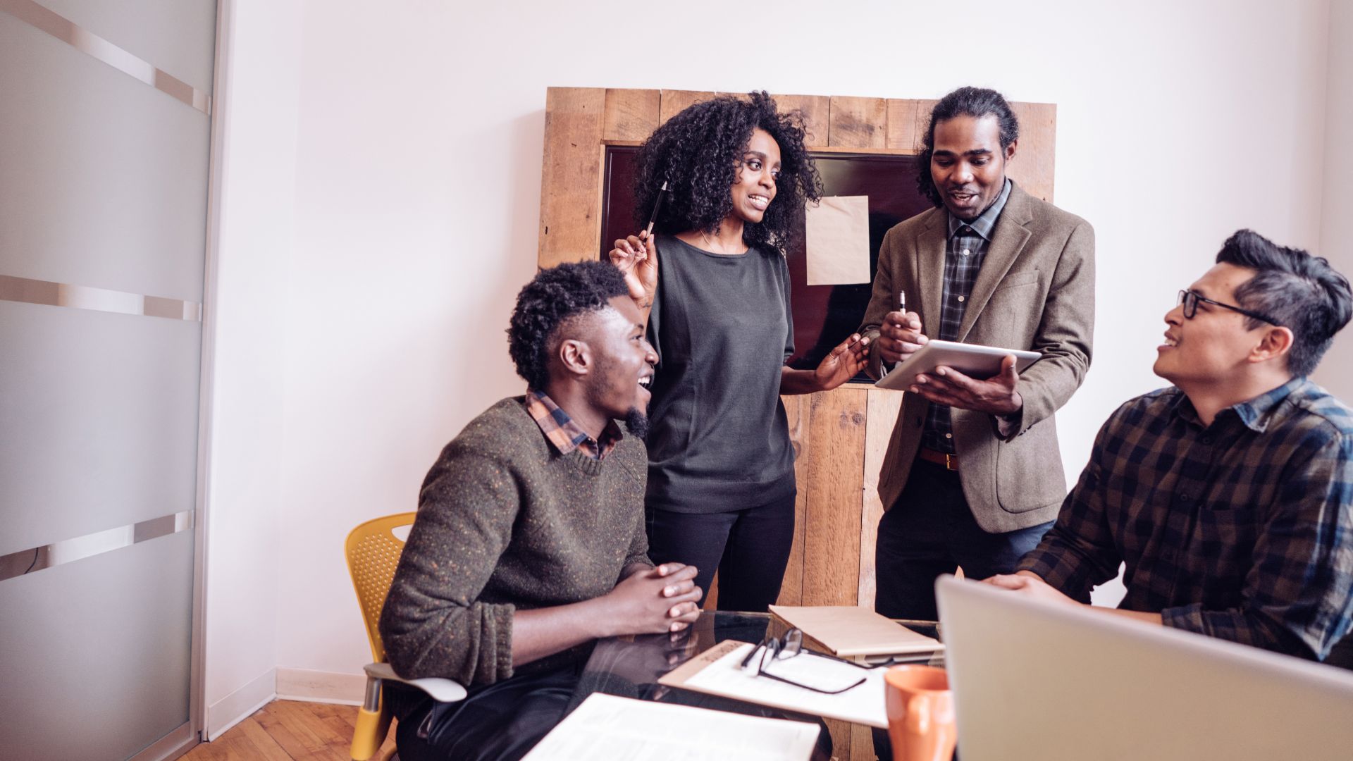 A diverse team of people are working around a desk. Some are standing, some are sitting. All are very animated and excited.