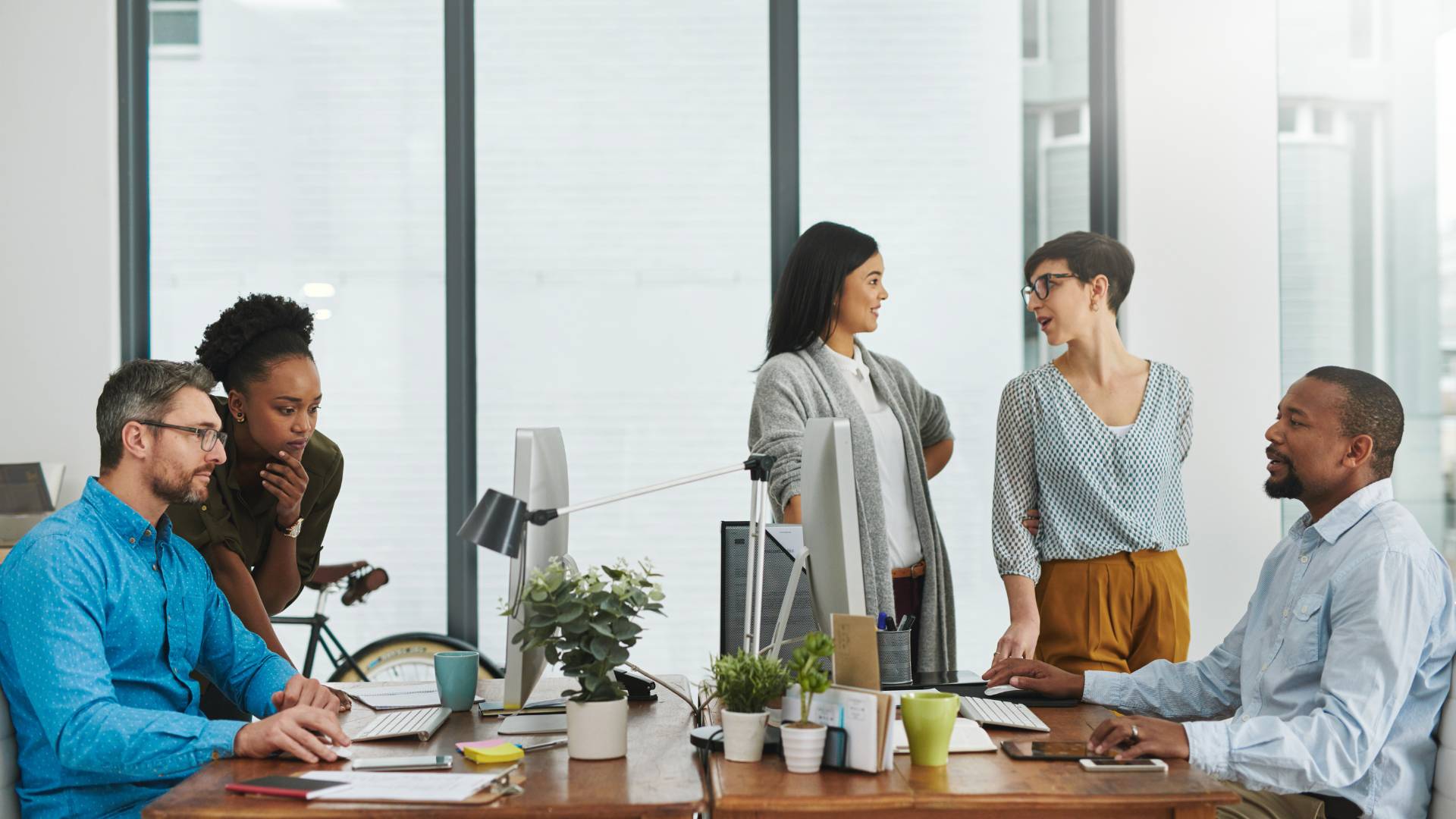 There are five employees in a conference room having a meeting at table.