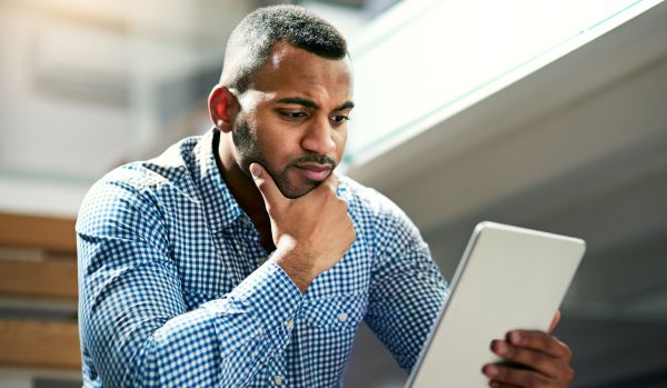 A man is sitting outside with his tablet trying to make a difficult decision.