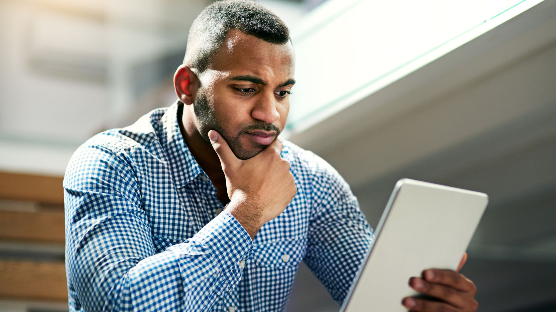 A man is sitting outside with his tablet trying to make a difficult decision.