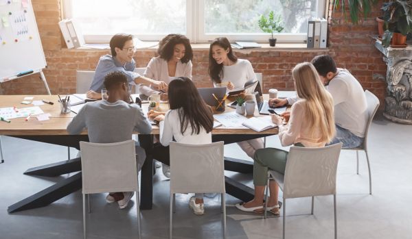 A diverse group of employees are working together on a project around a conference table with a window in the background.