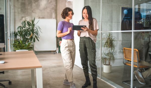 Two women are analyzing workforce trends on a tablet. They are standing in an office.