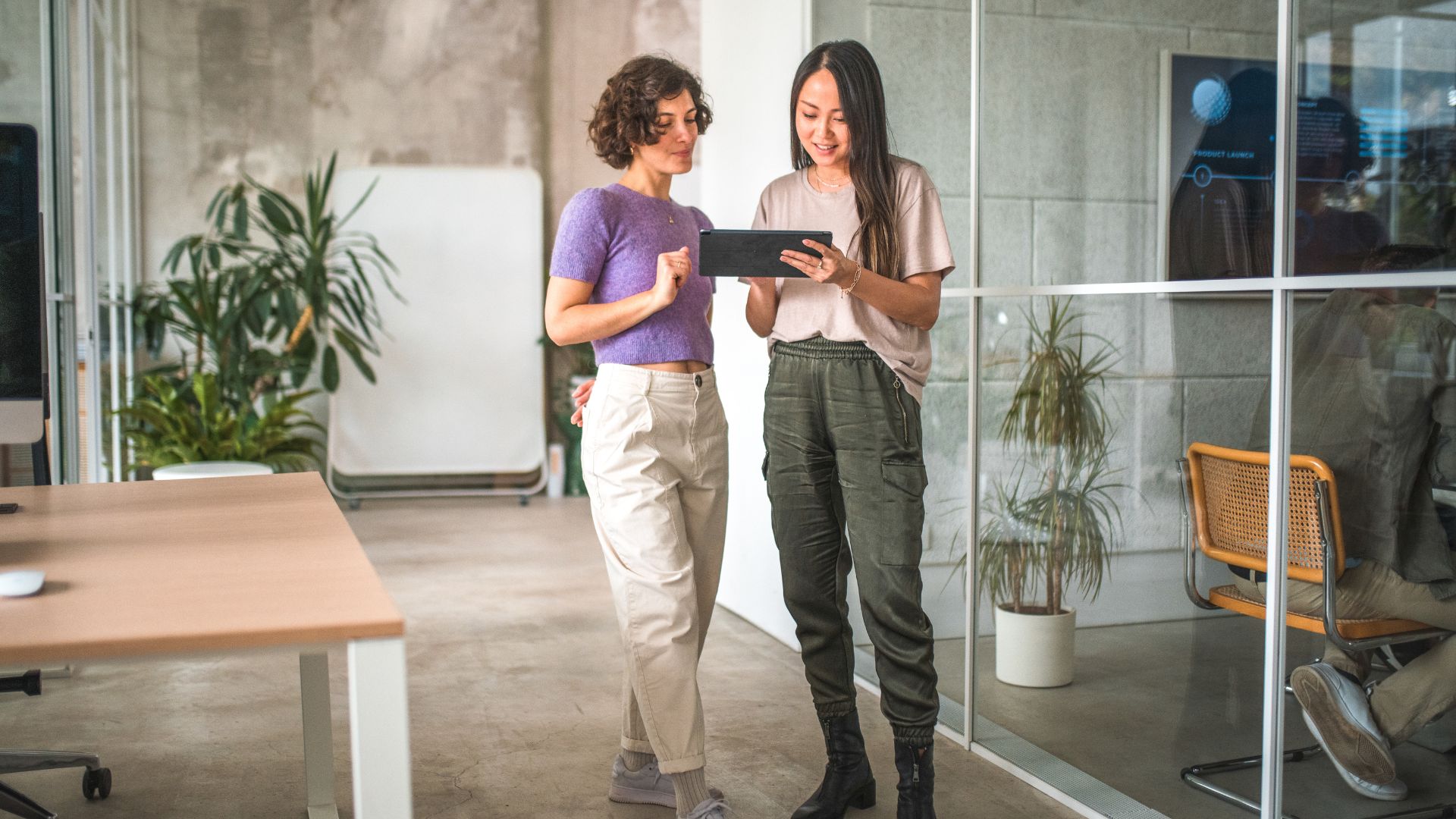 Two women are analyzing workforce trends on a tablet. They are standing in an office.