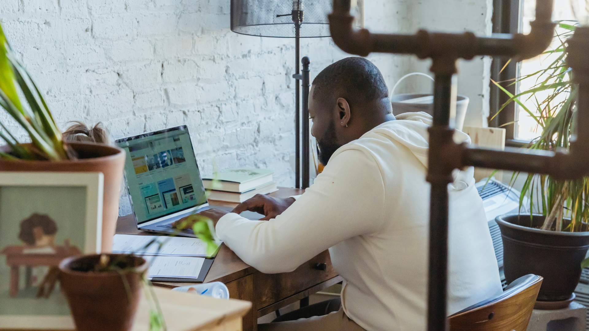 A young, black man sits at his desk working on his laptop.