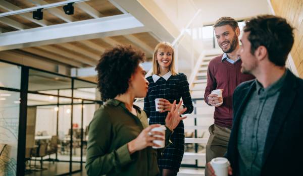 Four diverse employees are having a conversation in an office, smiling.