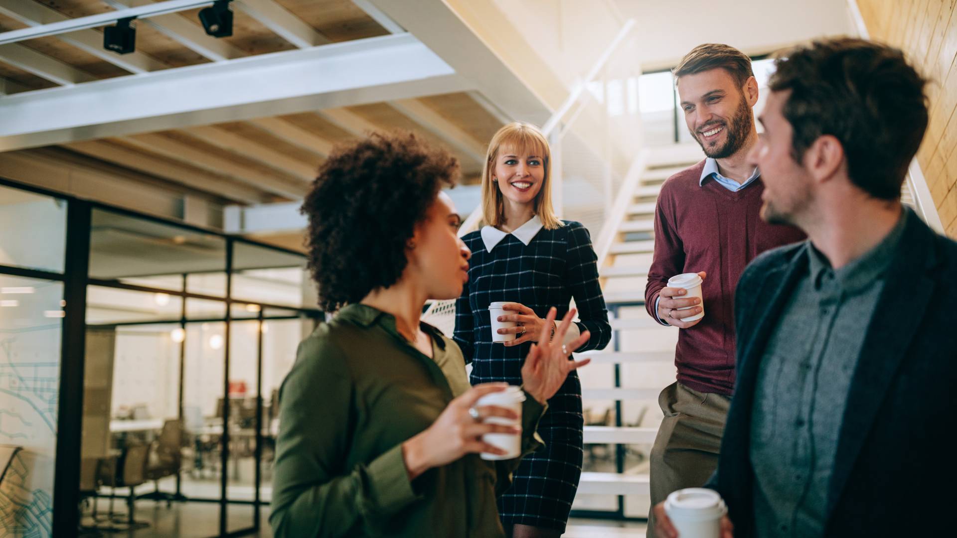 Four diverse employees are having a conversation in an office, smiling.