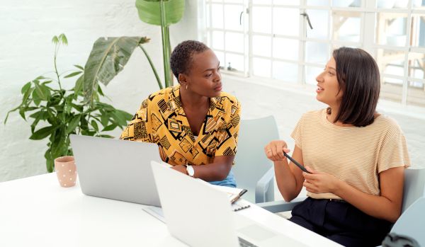 Two women are having a feedback conversation in a bright office space.