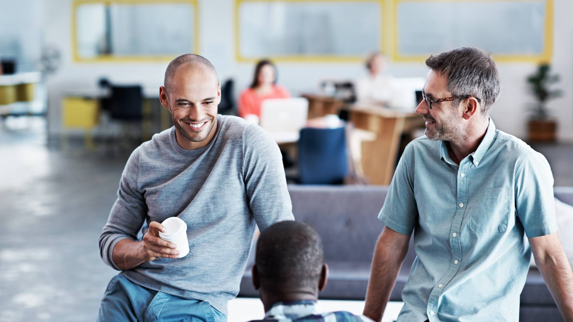 Three men are having a conversation in an open office space.