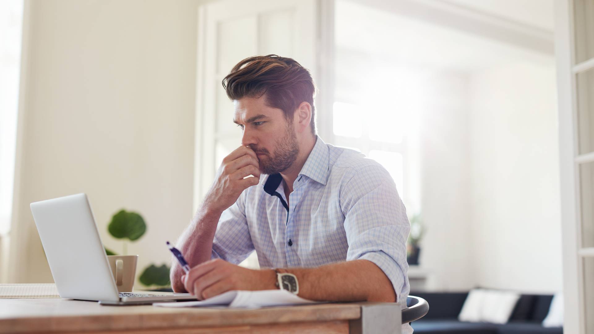 A man is working from home and looking at his laptop with a concerned look on his face.