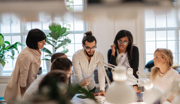 There are a group of seven people in an office gathered around a table working on an initiative.