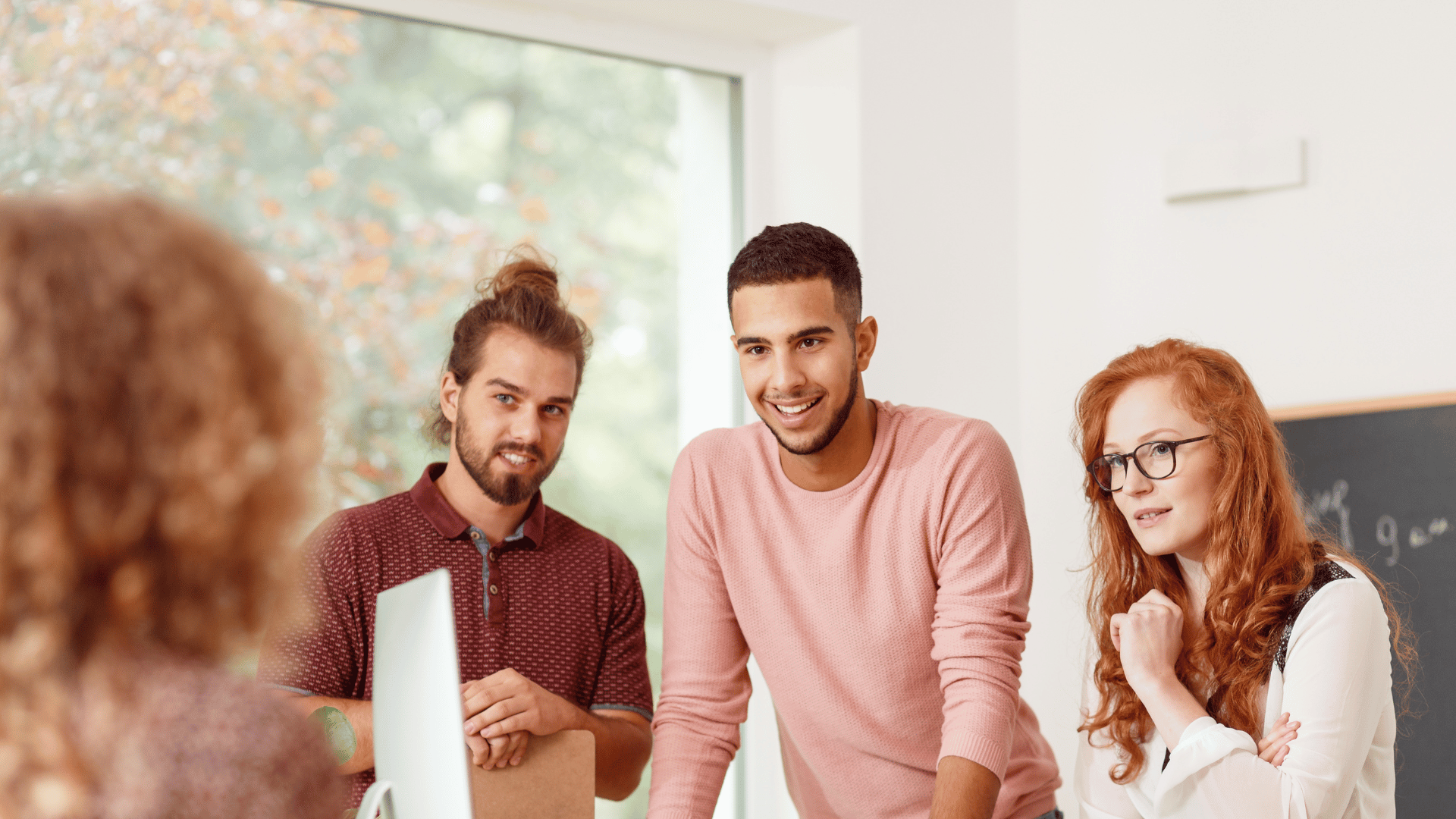 A group of 3 colleagues are looking at a 4th colleague. We can only see the back of the 4th colleague. They appear to be having a friendly discussion.