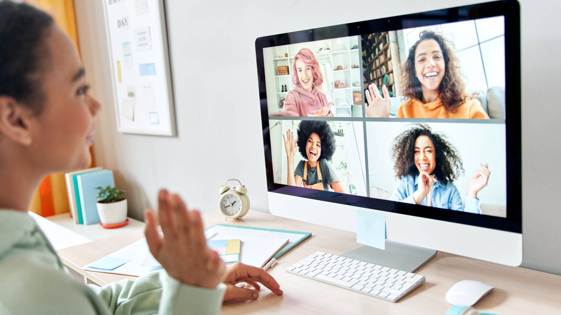 A woman is at home on her computer in a virtual meeting. There are four other women on the screen who are also in the virtual meeting.