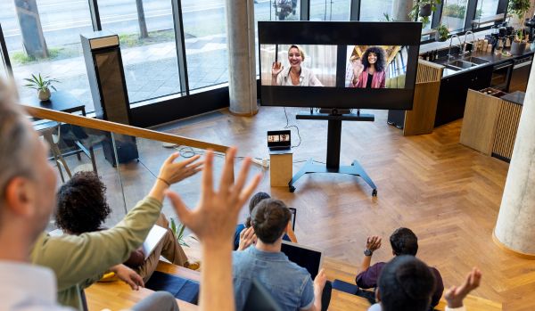 An in-office team is waving at remote workers who are video-ing into their event.
