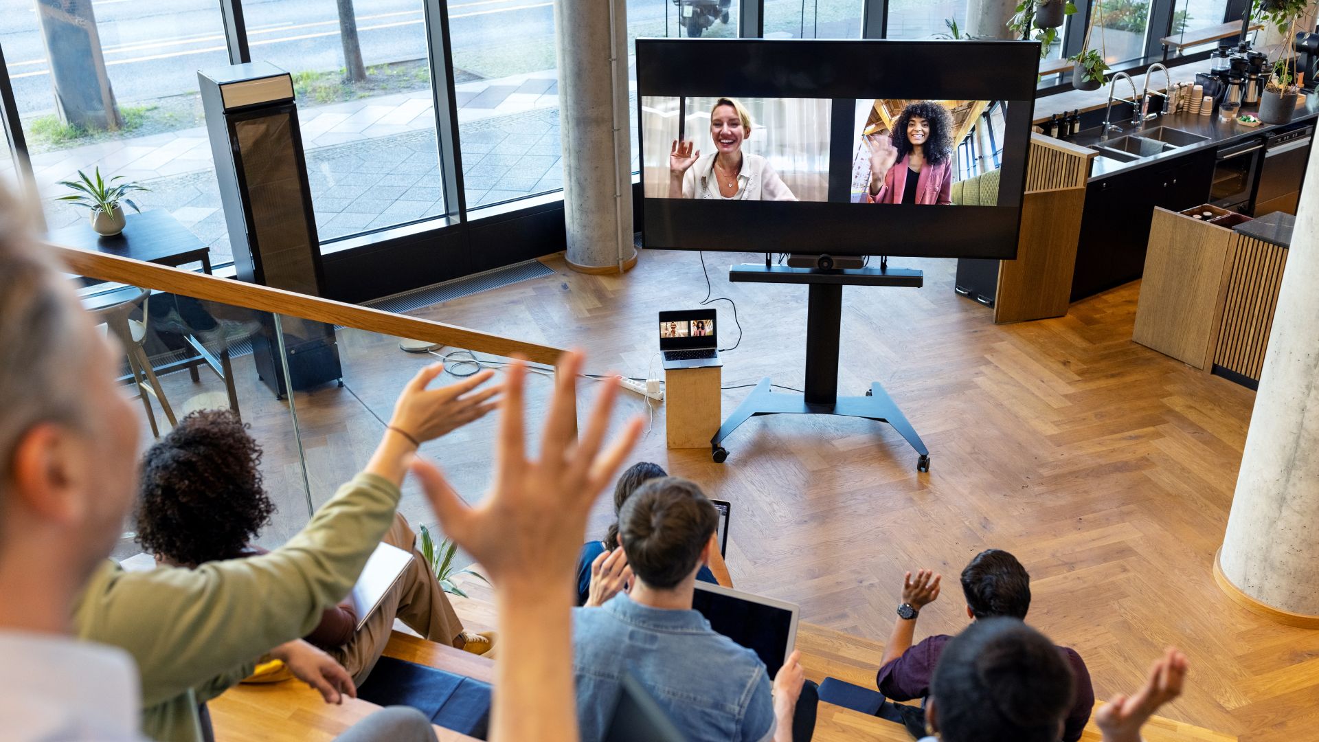 An in-office team is waving at remote workers who are video-ing into their event.