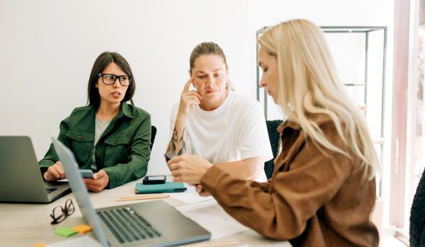 A diverse group of people are sitting at a table with their laptops, discussing how AI is impacting their learning strategy.