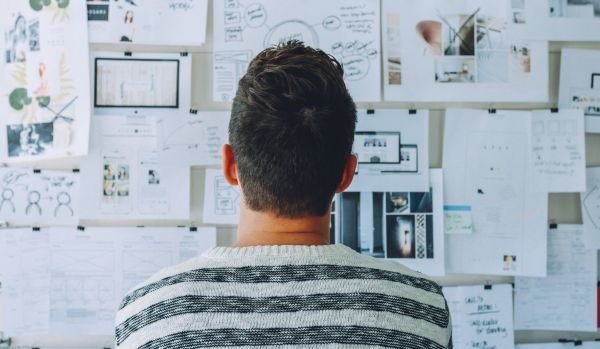 A man is standing in front of a board covered in brainstorming ideas. We are looking at the man's back.