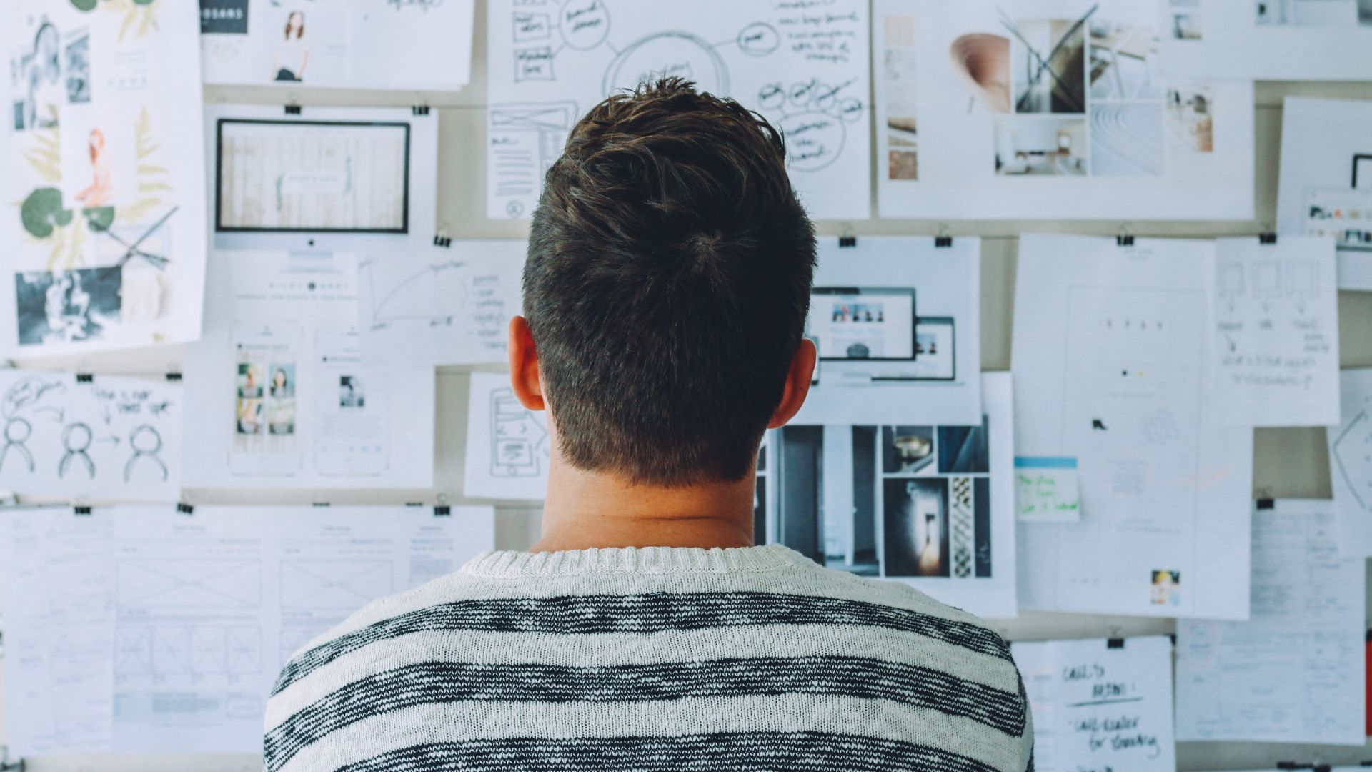 A man is standing in front of a board covered in brainstorming ideas. We are looking at the man's back.