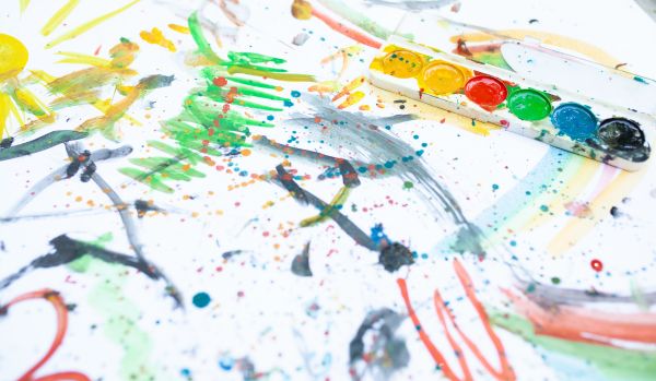 We're looking at a paper where a child has used watercolors to paint "outside the lines". There are brushes and a palette on the right side of the frame.