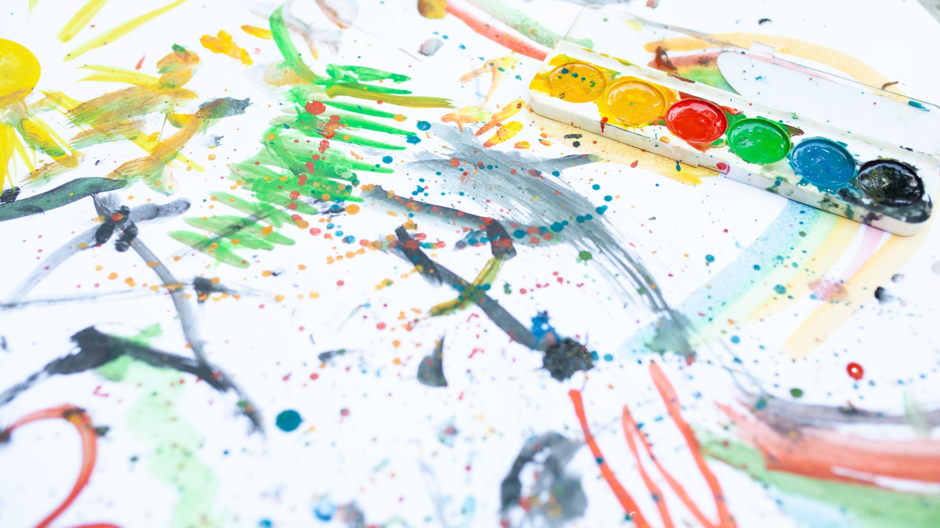 We're looking at a paper where a child has used watercolors to paint "outside the lines". There are brushes and a palette on the right side of the frame.