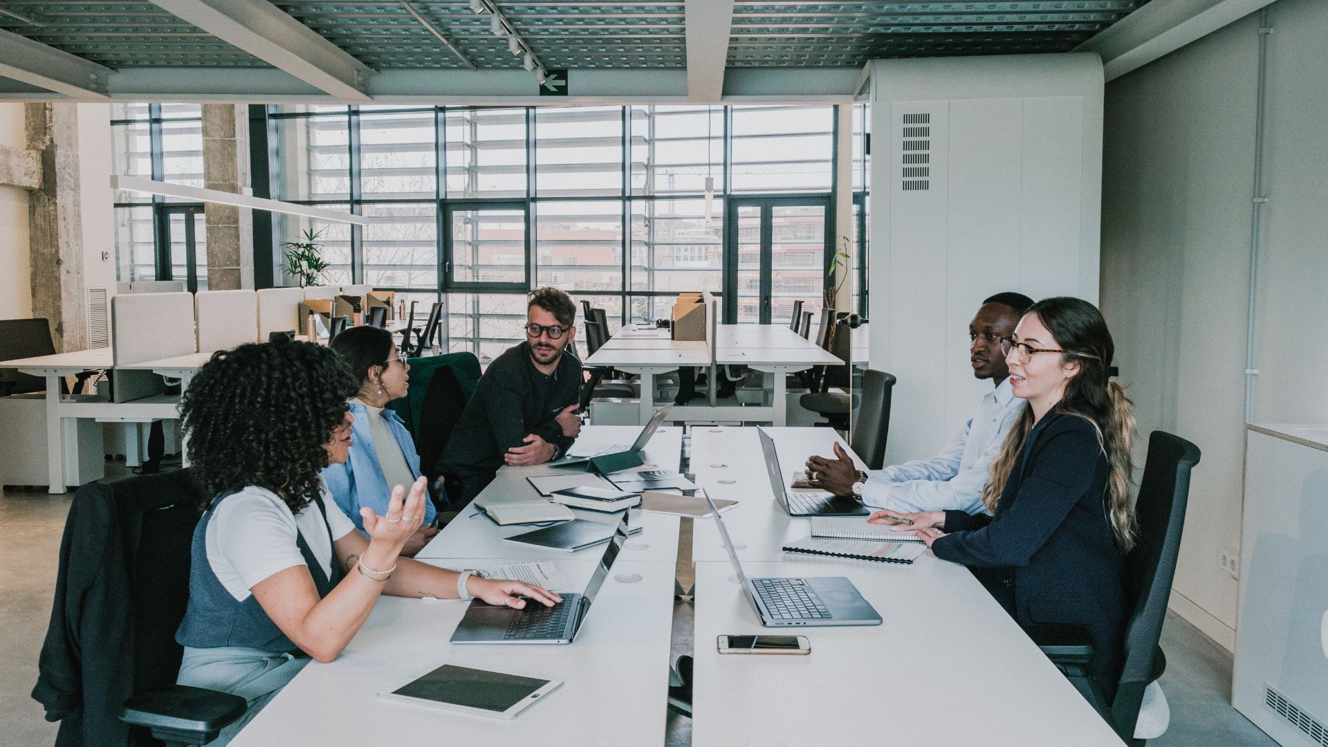A diverse team of people are working around a conference table and having conversations.