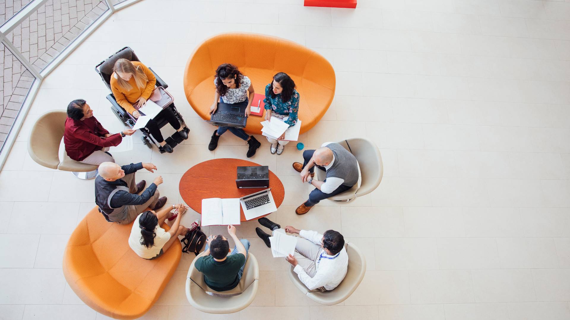 We are looking down from overhead at a diverse group of employees having a discussion in a sitting area.