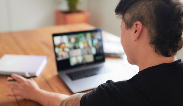 We're looking over the shoulder of a non-binary person at their laptop screen where they are participating in a live, virtual training course.