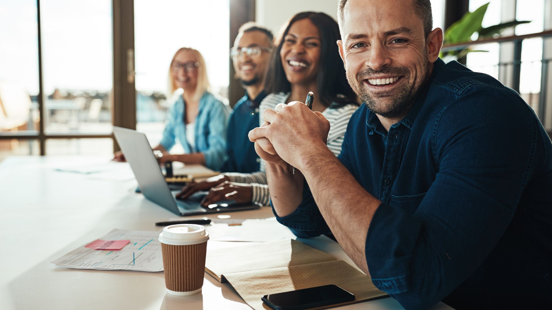 A happy diverse team of people are sitting at a table smiling at the camera.