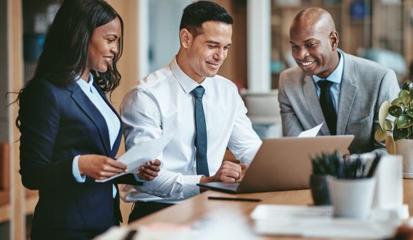 A diverse team of 3 people are looking at a laptop and discussing learning plans.