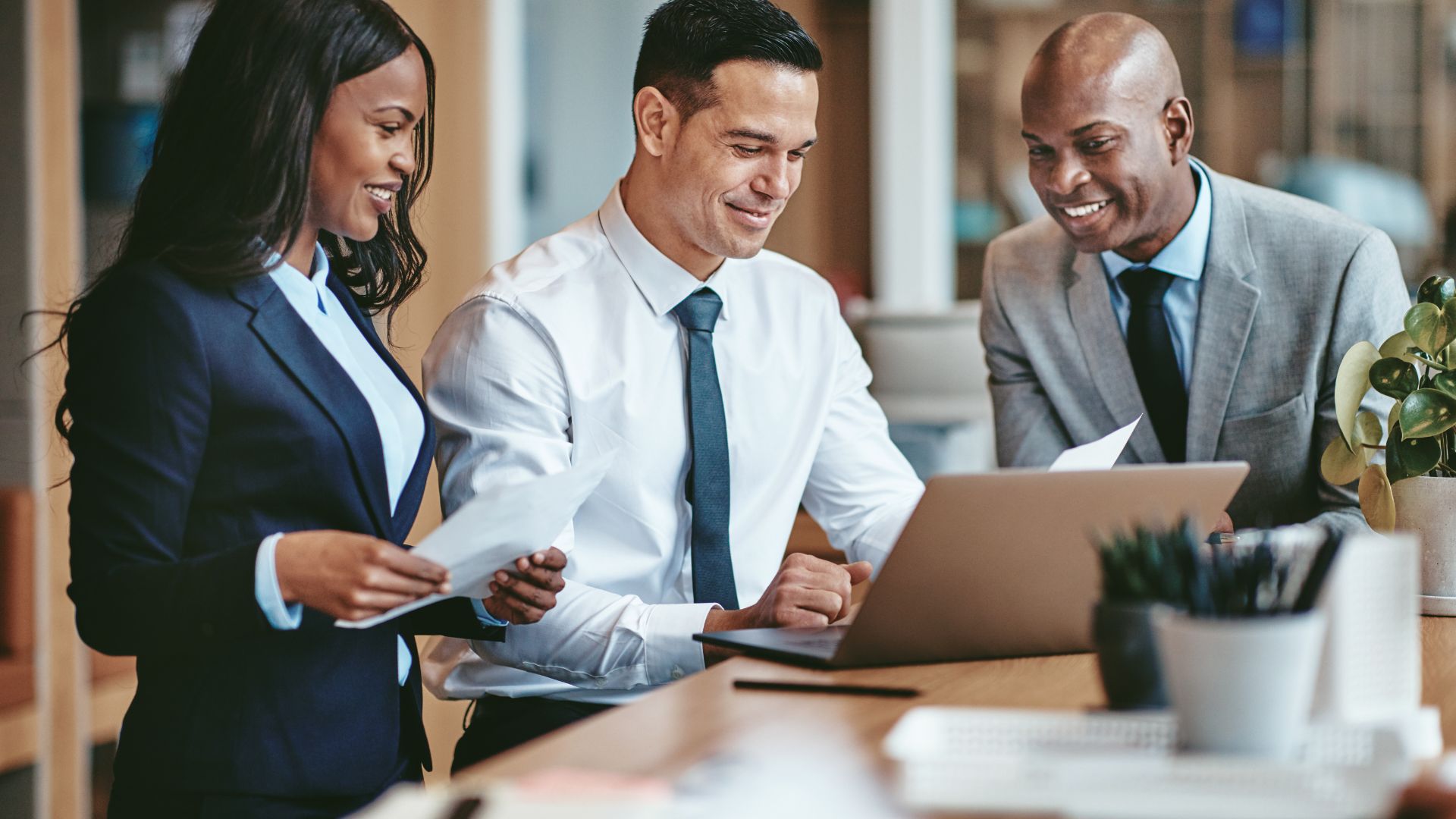 A diverse team of 3 people are looking at a laptop and discussing learning plans.