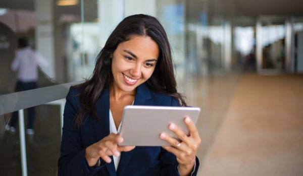A young woman is smiling at her tablet in an open office space.