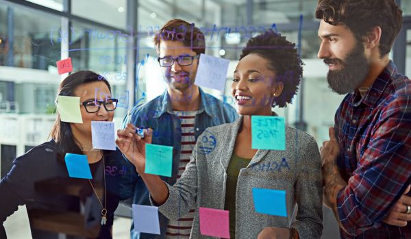 We're looking through a transparent whiteboard at a diverse learning and development team using markers and post-its to create a learning roadmap.