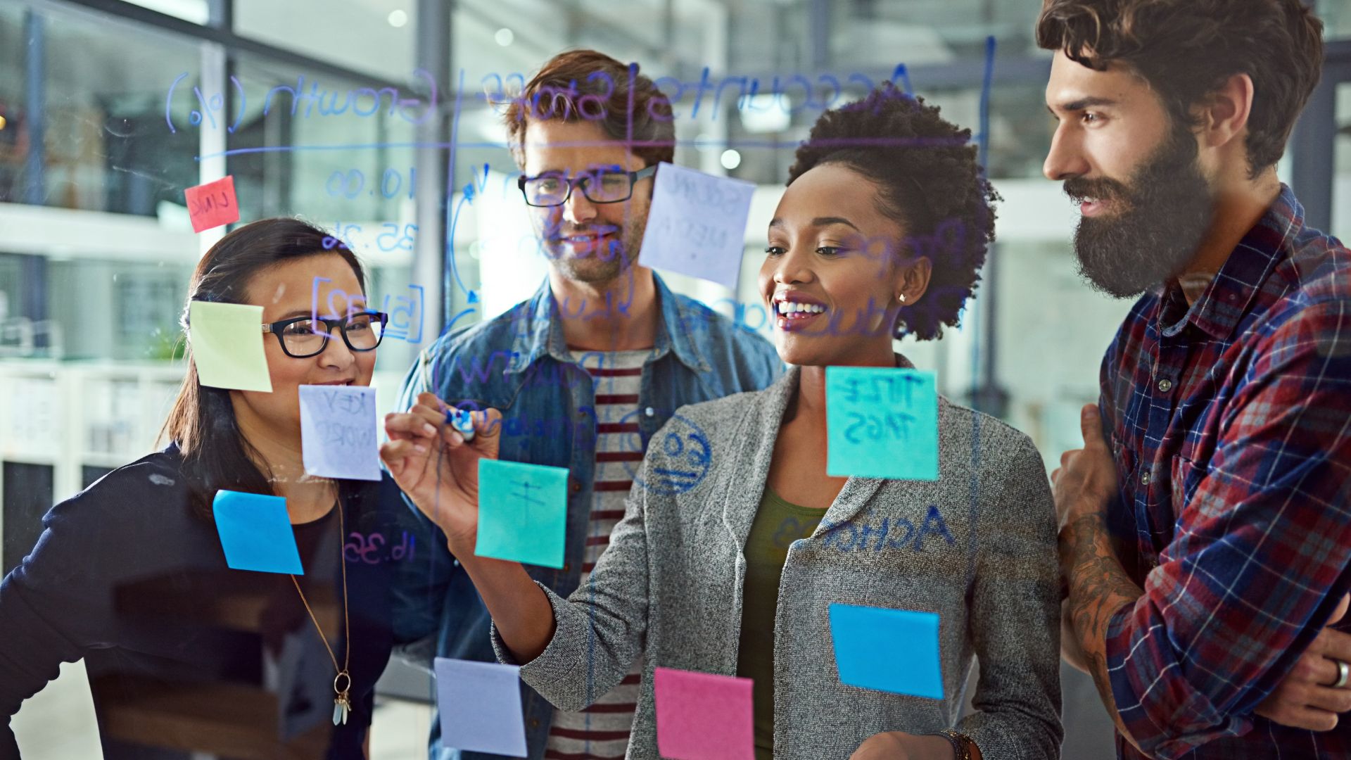 We're looking through a transparent whiteboard at a diverse learning and development team using markers and post-its to create a learning roadmap.