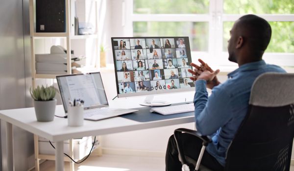 A man is participating in a live virtual workshop from his home office. We're looking over his shoulder from behind at his monitor.