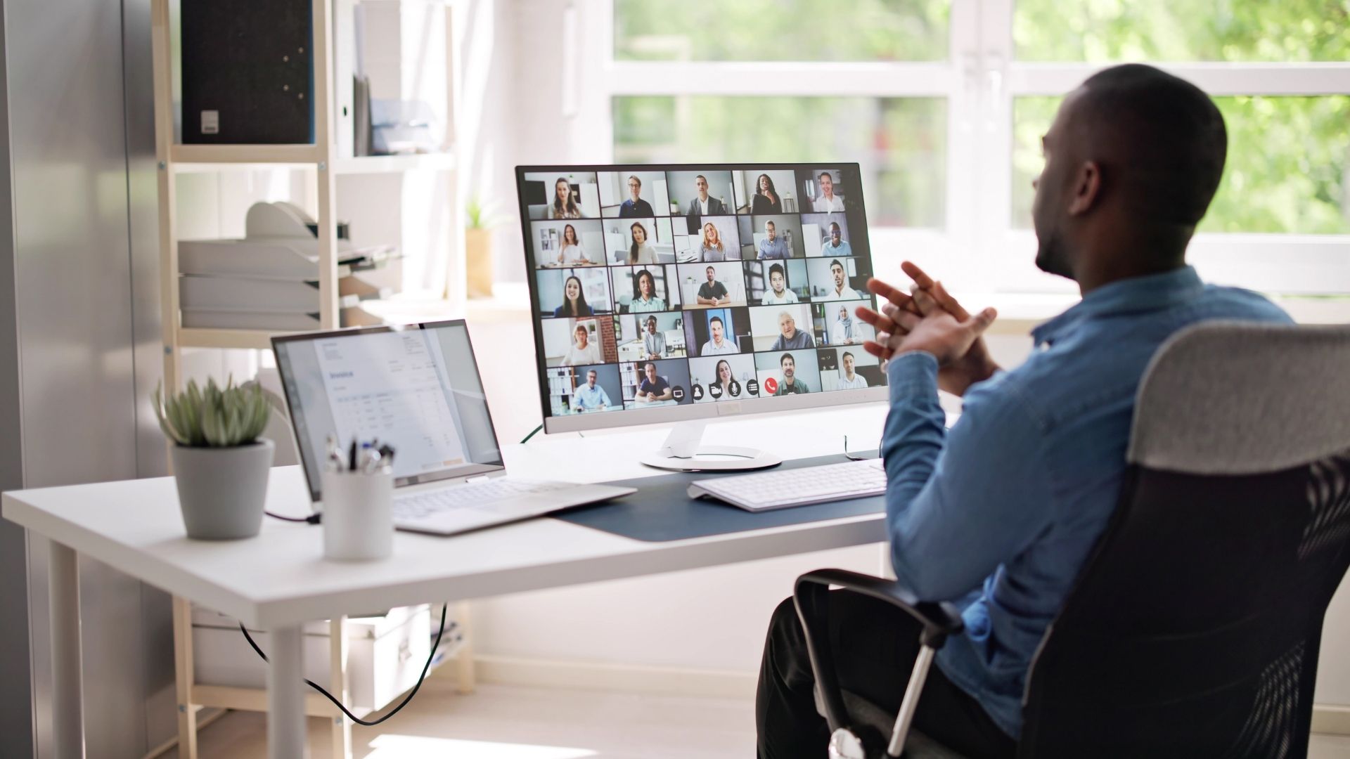 A man is participating in a live virtual workshop from his home office. We're looking over his shoulder from behind at his monitor.