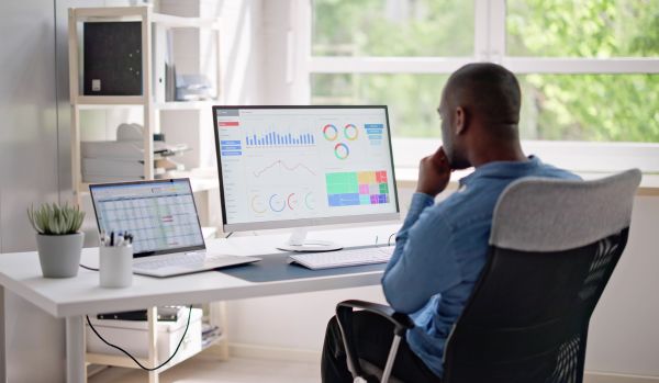 We're looking over the shoulder of a man reviewing a data dashboard on his monitor in his home office.