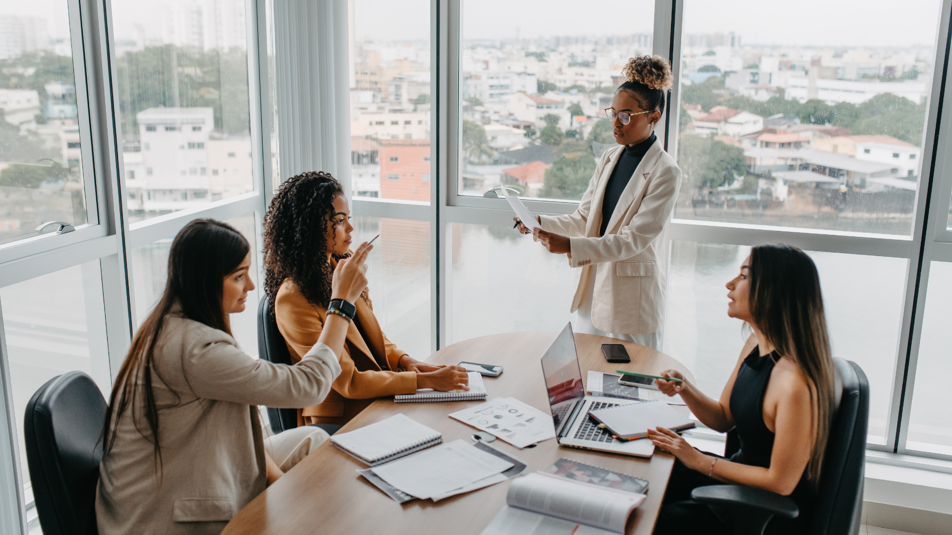 A female presenting leadership team is working together in a conference room with many windows.