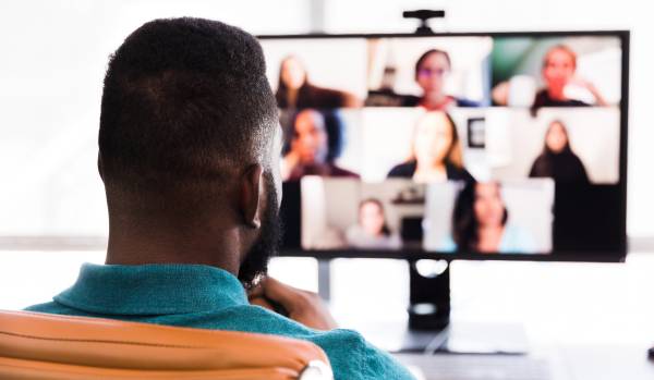 We are looking over a man's shoulder at his computer monitor where he is participating in a virtual live learning session.