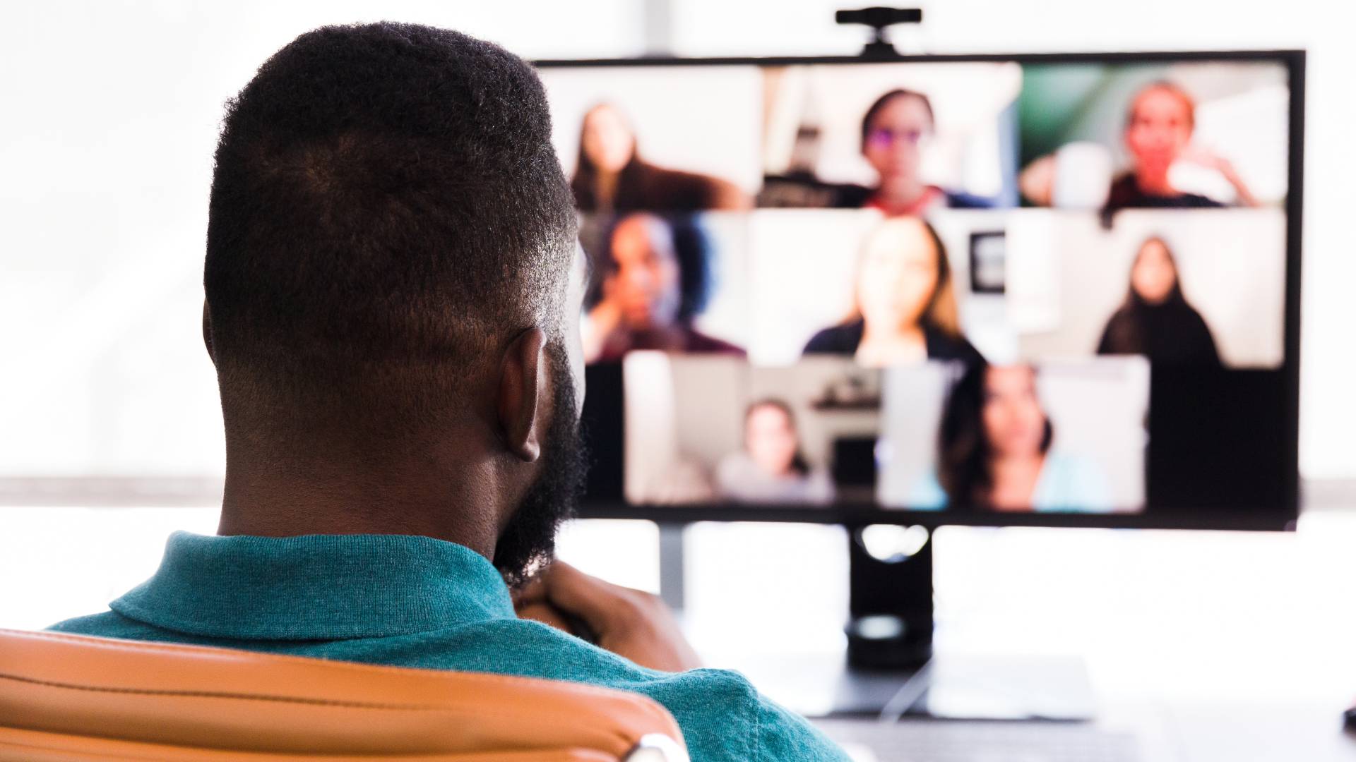 We are looking over a man's shoulder at his computer monitor where he is participating in a virtual live learning session.