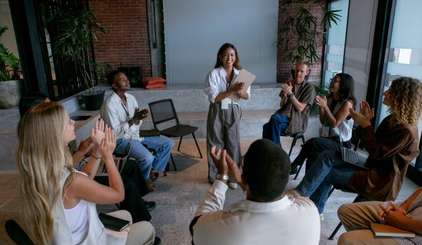 A woman is standing and presenting to her colleagues. Her colleagues are having a conversation in a circle.