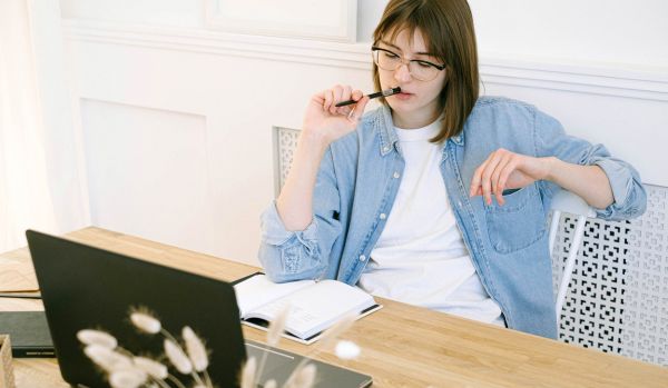 A manager is sitting at a table with her laptop and notebook, thinking hard about how to give clear feedback.