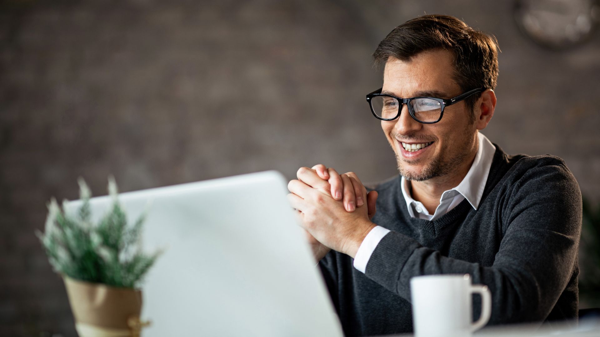 A young man in glasses id smiling down at his laptop screen.