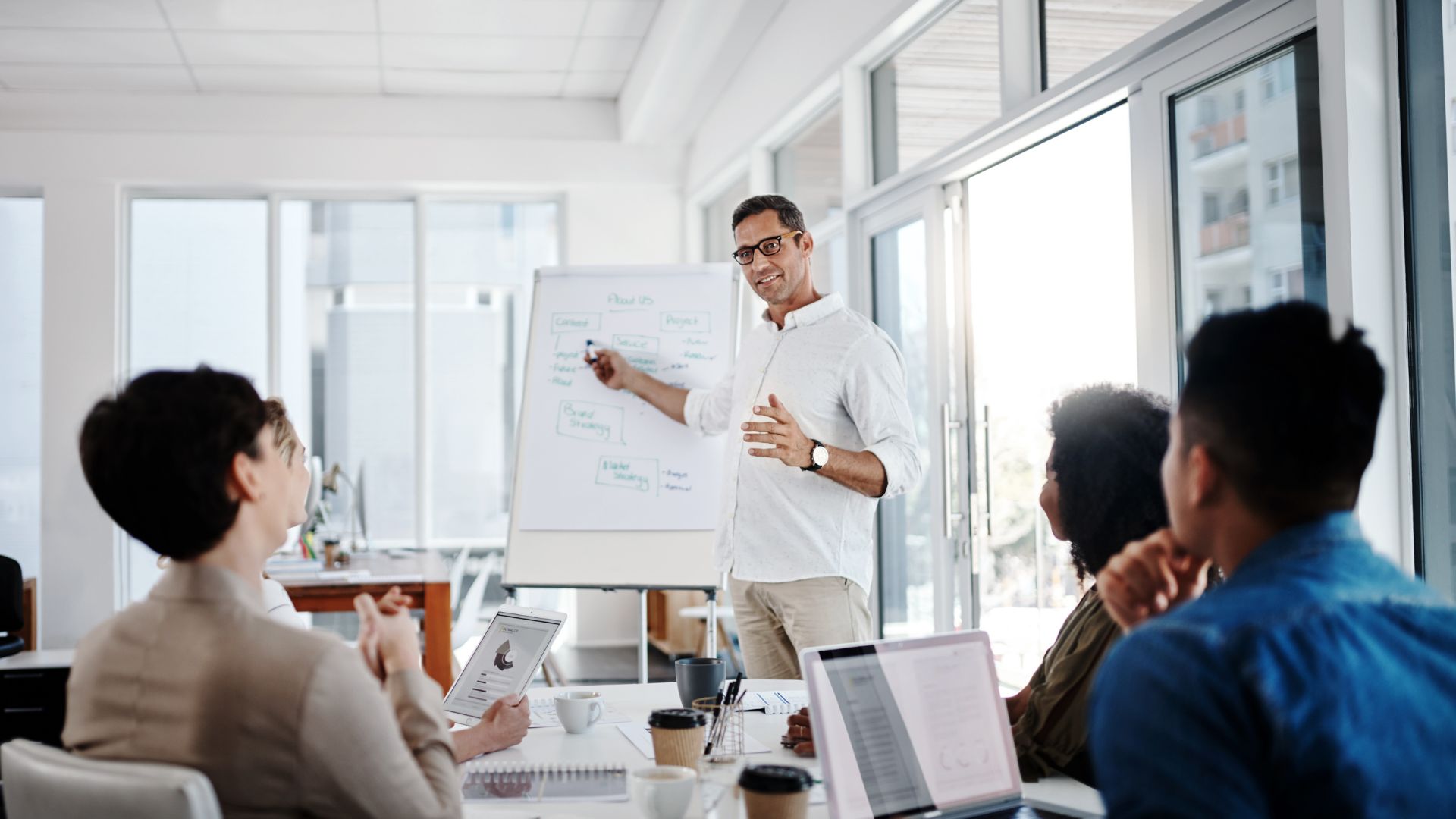 A man is standing at a flip chart leading a team meeting.