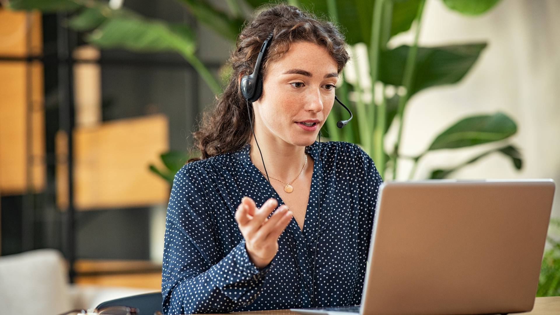 A young woman has a headset on and is having a conversation with someone via video conference.