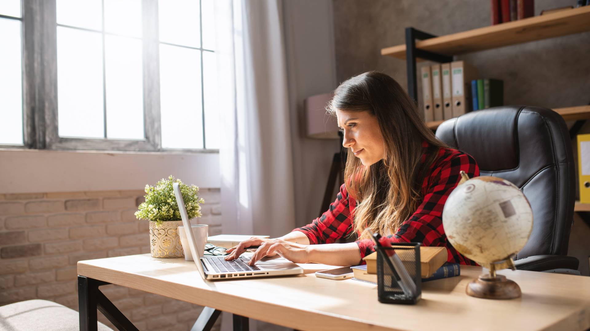We're looking at the profile of a woman working on her laptop at her home office.