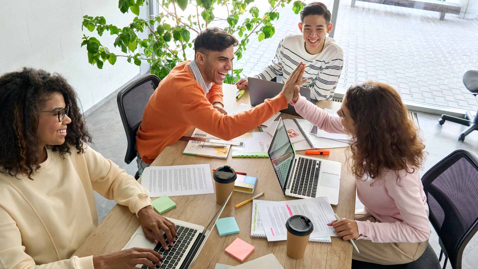 Young happy team collaborating around a table. Two of them are high-fiving.