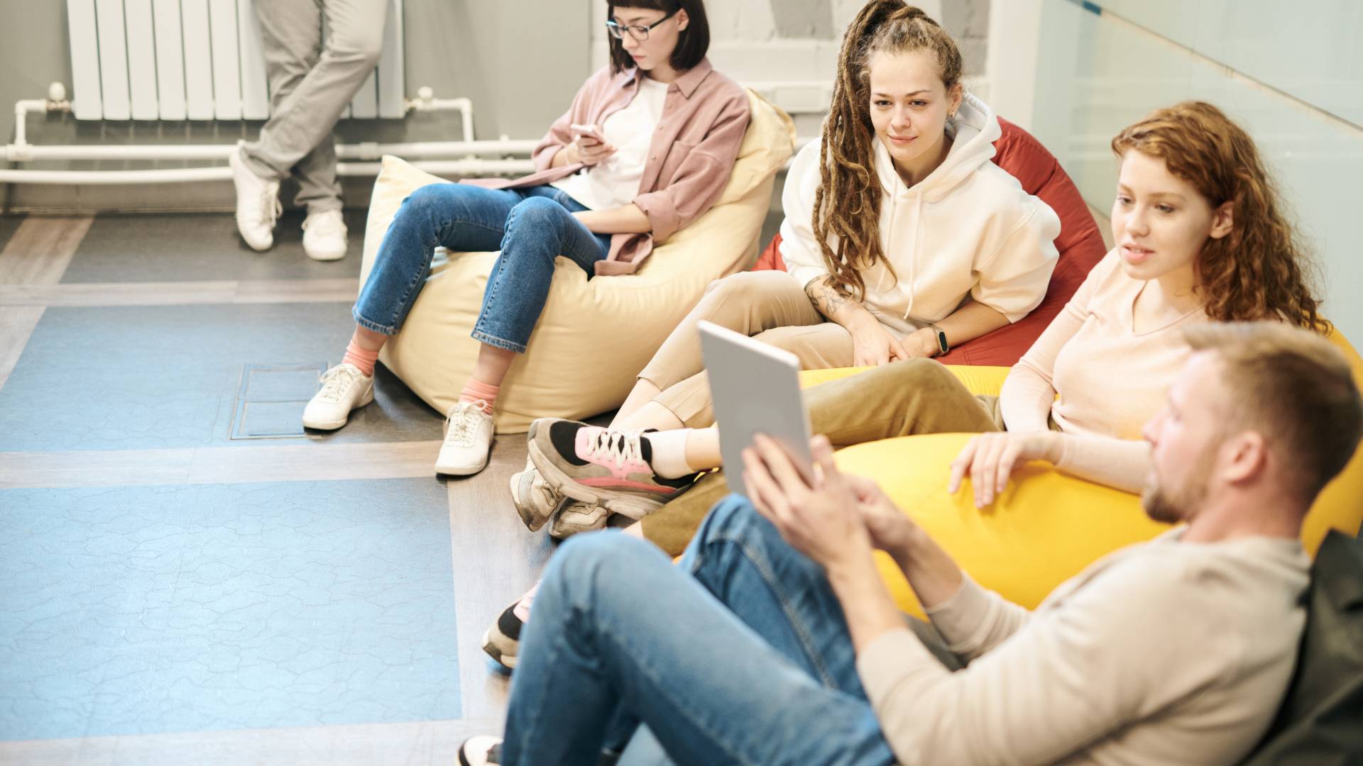 A group of employees sitting on bean bag chairs in an office. They're looking at an iPad.