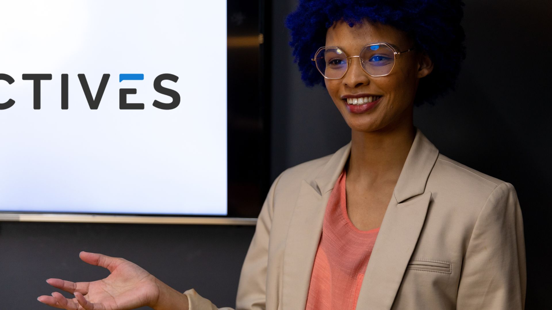 A confident professional with blue hair and glasses presents in front of a screen displaying the Electives logo. This image reflects the enthusiasm and engagement encouraged in the blog post about launching a small-budget L&D program. The presenter's demeanor emphasizes the importance of leadership and manager involvement in promoting and participating in learning opportunities within the organization.